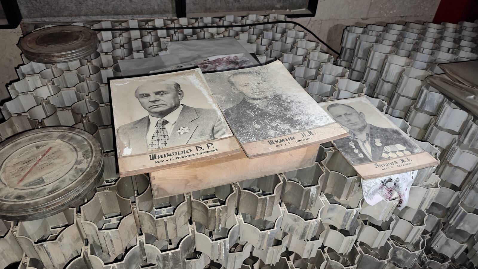 Портреты передовиков кто-то положил на стопку легких алюминиевых решеток. Раньше эти конструкции украшали потолок в административном корпусе завода.