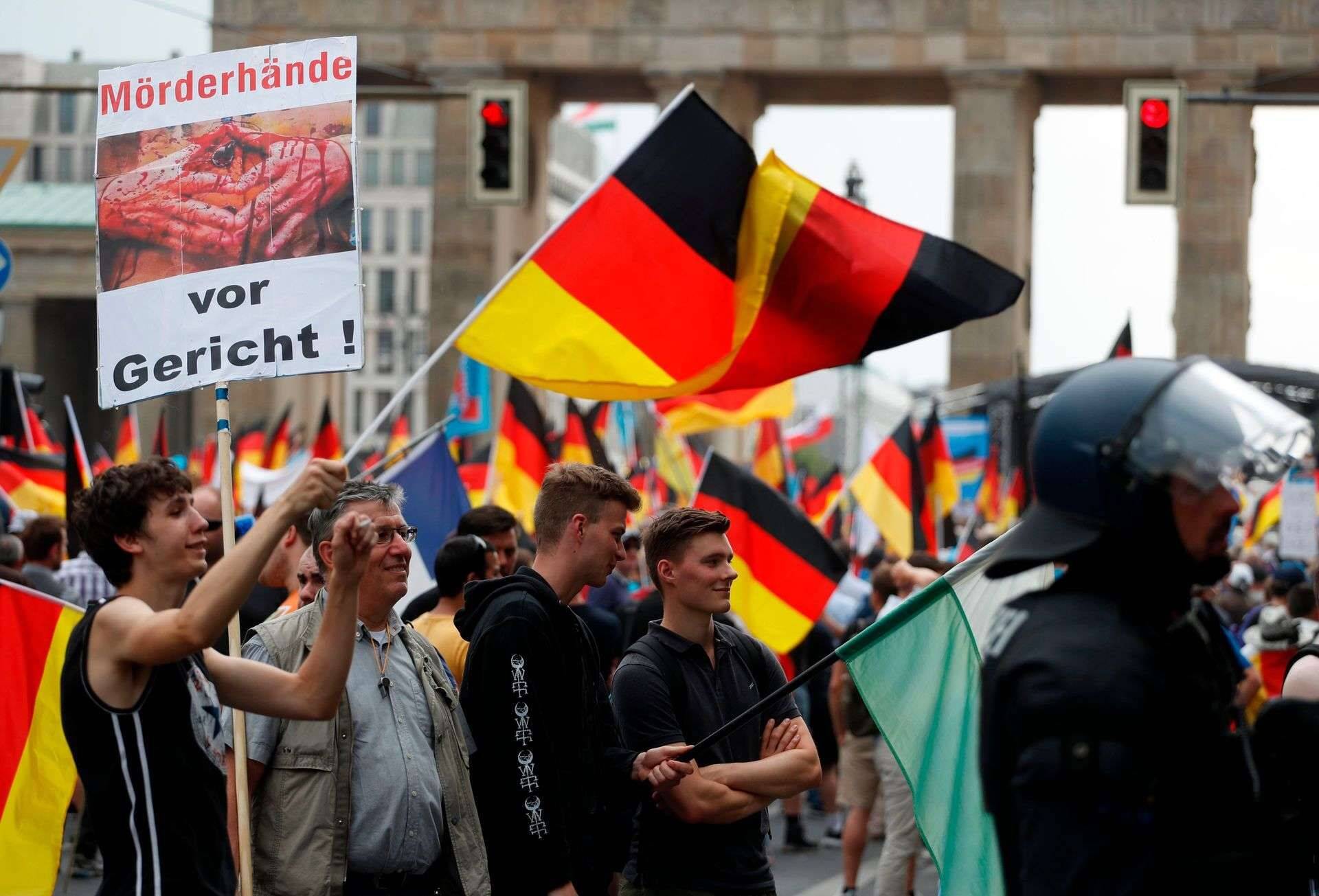 Alternative for Germany (AfD)'s demonstrators wave German flags and hold a placard reading "Killers Hands in trial!" in front of the Brandenburg Gate (Brandenburger Tor) in Berlin during the "demonstration for the future of Germany" called by the far-right AfD in Berlin on May 27, 2018. The police estimates 2000 to 2500 people attending the AfD demonstration in Berlin. / AFP PHOTO / Odd ANDERSEN