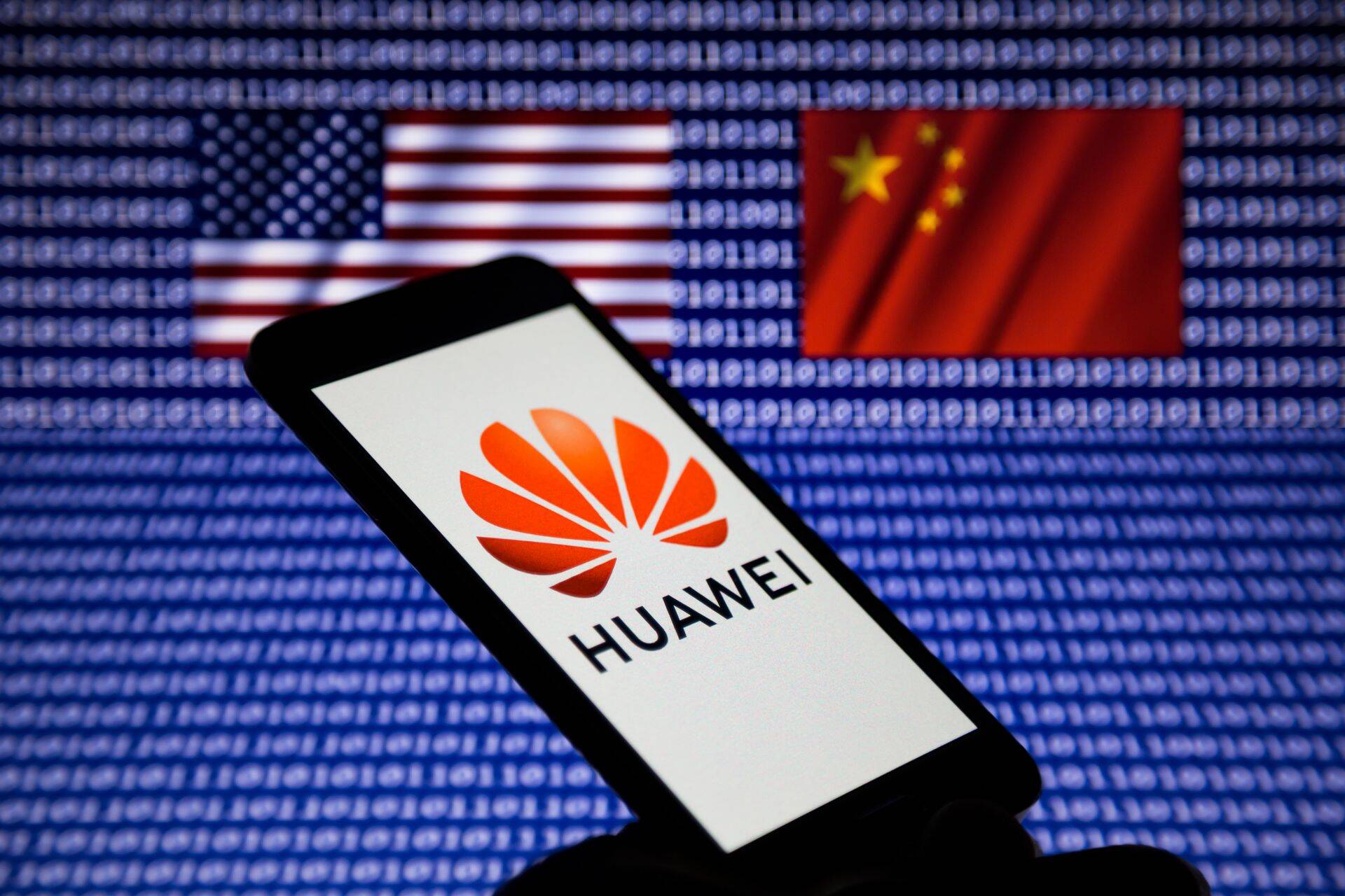 Illustration photo - Logo of Huawei is displayed on a smartphone backdropped by the waving flags of United States and China, with binary code digits on screen.