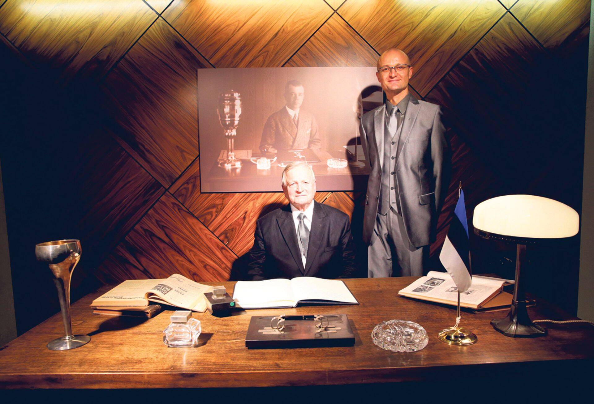 Seinal on kullaseppmeister Roman Tavasti pilt. Töölaua taga istub tema 1933. aastal sündinud poeg Raul Tavast ja seisab 1969. aastal sündinud pojapoeg Arvi Tavast.