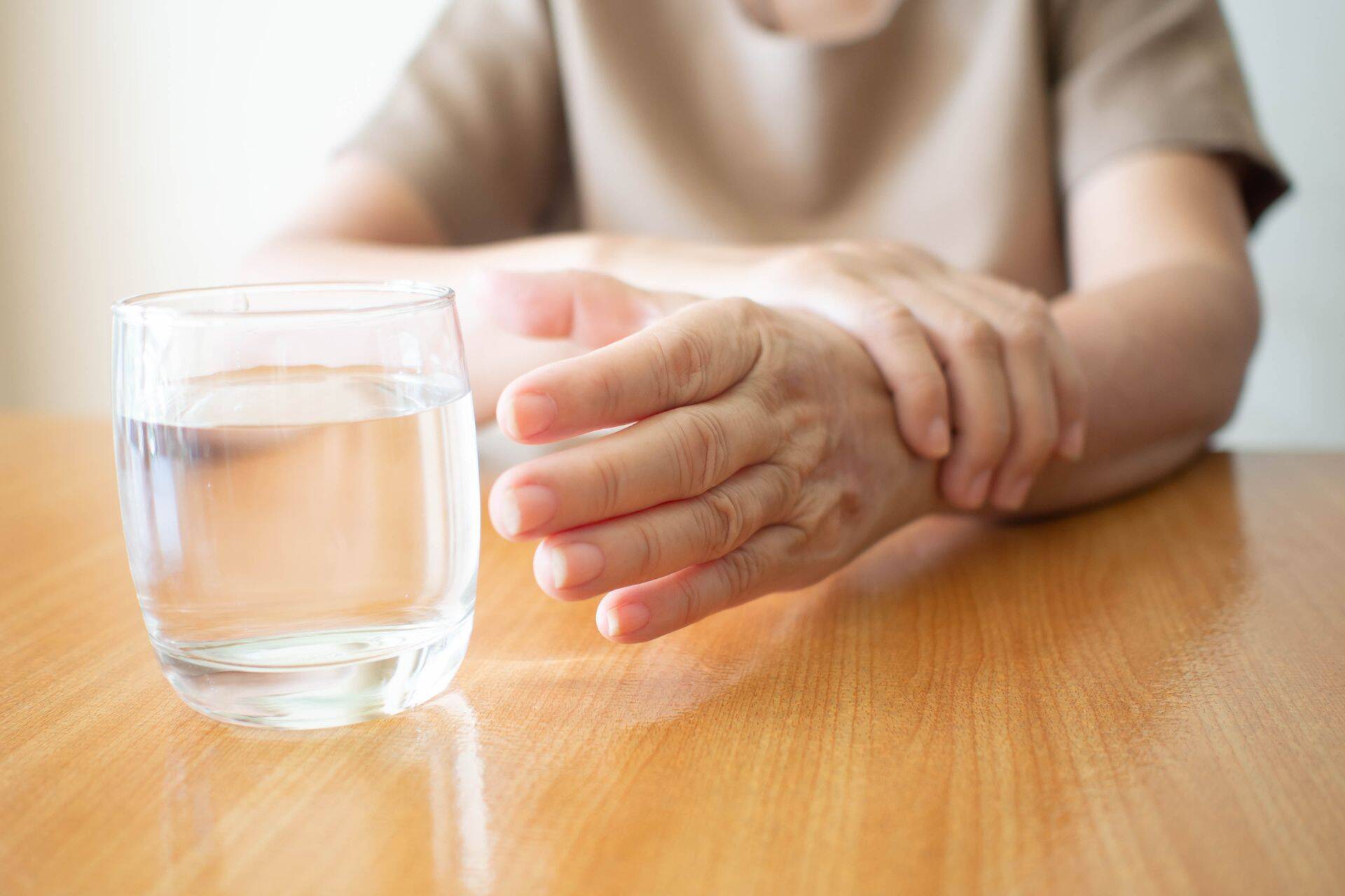 Parkinsoni tõvega naine joogiklaasi võtmas teise käe abil.